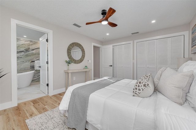 bedroom featuring ceiling fan, connected bathroom, light hardwood / wood-style floors, a textured ceiling, and two closets