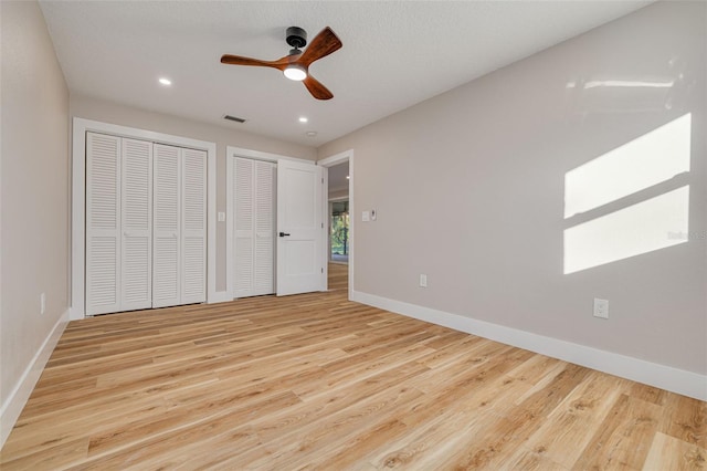 unfurnished bedroom featuring two closets, light hardwood / wood-style floors, and ceiling fan