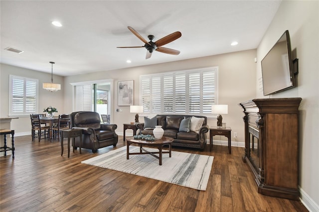 living room with ceiling fan with notable chandelier and dark hardwood / wood-style flooring