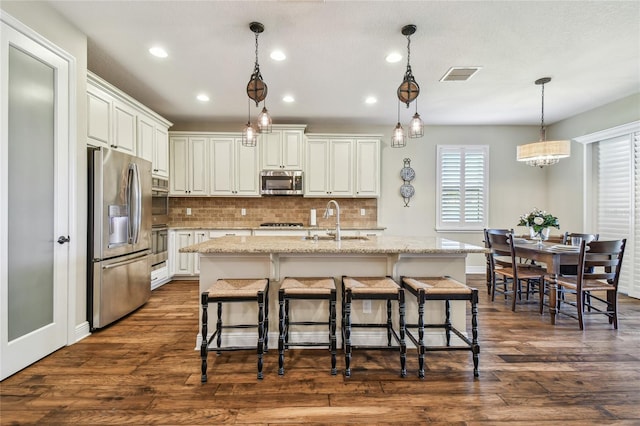 kitchen with a center island with sink, hanging light fixtures, dark hardwood / wood-style floors, and appliances with stainless steel finishes