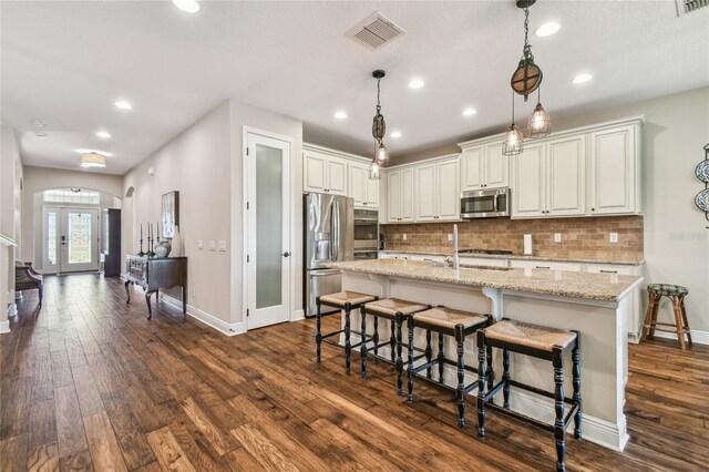 kitchen with white cabinetry, dark wood-type flooring, light stone counters, an island with sink, and appliances with stainless steel finishes