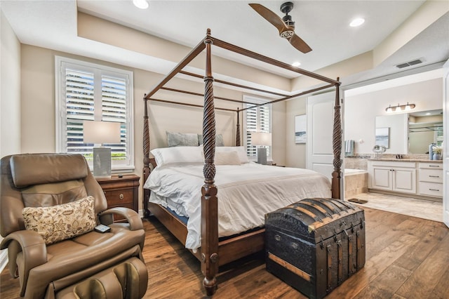 bedroom with ceiling fan, a raised ceiling, wood-type flooring, and ensuite bath