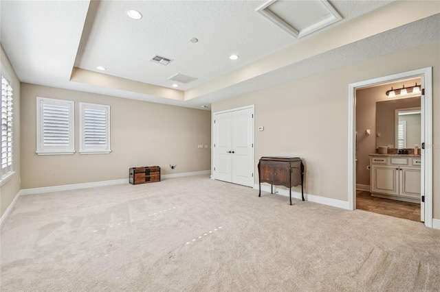 unfurnished bedroom with a raised ceiling, ensuite bathroom, light colored carpet, and a textured ceiling