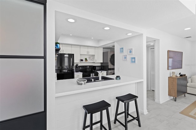 kitchen featuring white cabinets, black appliances, sink, stacked washer / drying machine, and a kitchen bar