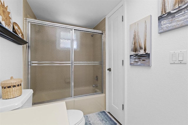 bathroom featuring combined bath / shower with glass door and toilet