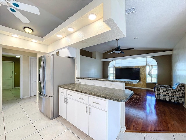 kitchen with kitchen peninsula, stainless steel fridge, vaulted ceiling, light tile patterned floors, and white cabinetry