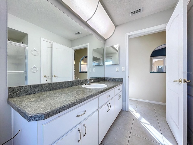 bathroom with tile patterned floors, vanity, a textured ceiling, and walk in shower