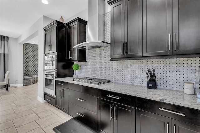 kitchen with backsplash, light stone countertops, wall chimney range hood, and stainless steel appliances