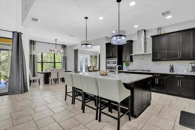 kitchen featuring wall chimney exhaust hood, hanging light fixtures, an island with sink, and a breakfast bar