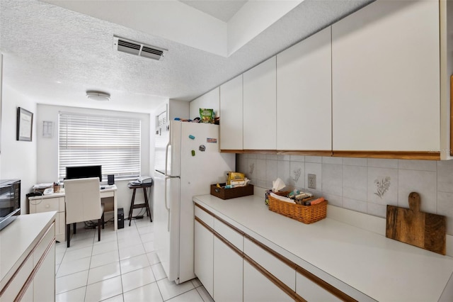 kitchen with light tile patterned floors, a textured ceiling, white cabinets, and white refrigerator