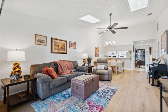 living room with ceiling fan with notable chandelier, a textured ceiling, light hardwood / wood-style flooring, and a skylight