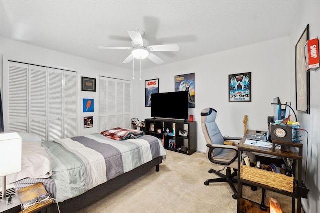 bedroom with ceiling fan, light colored carpet, and multiple closets