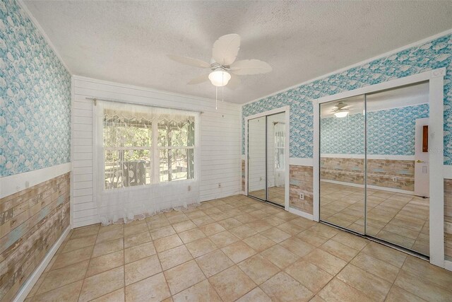 unfurnished bedroom featuring a textured ceiling, two closets, ceiling fan, and ornamental molding