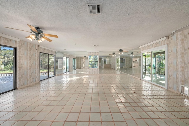 unfurnished room with a textured ceiling, ceiling fan, a healthy amount of sunlight, and wood walls