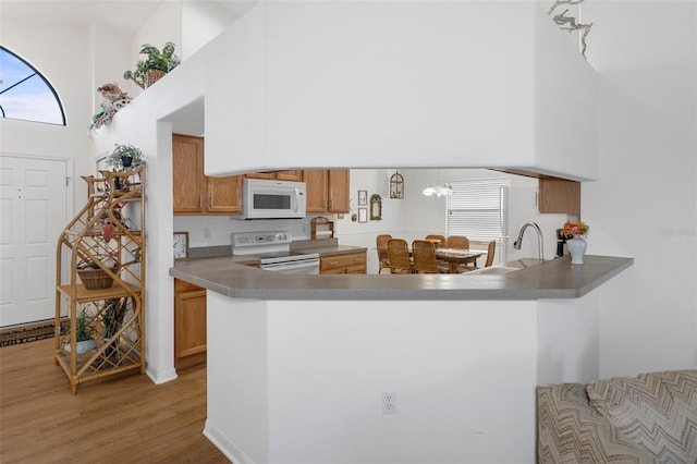 kitchen featuring white appliances, an inviting chandelier, a towering ceiling, light hardwood / wood-style floors, and kitchen peninsula