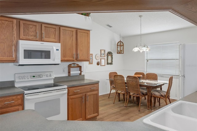 kitchen with hanging light fixtures, a chandelier, lofted ceiling, light hardwood / wood-style floors, and white appliances