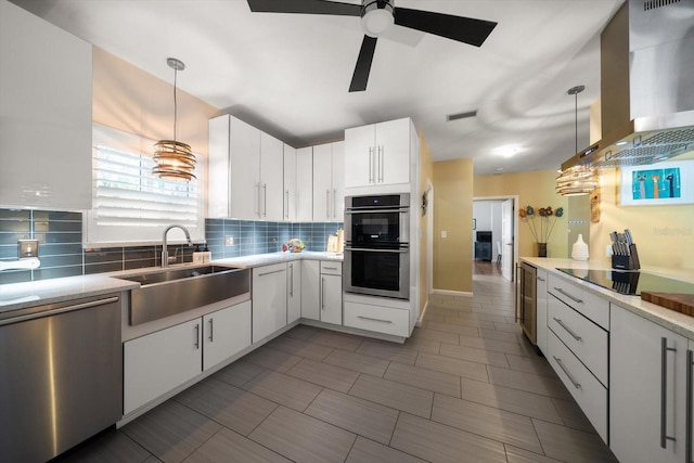 kitchen with sink, wall chimney exhaust hood, hanging light fixtures, white cabinets, and appliances with stainless steel finishes