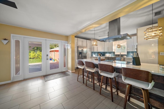 kitchen with backsplash, black electric stovetop, stainless steel fridge, decorative light fixtures, and island exhaust hood