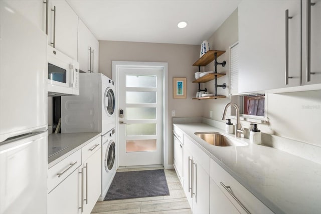 kitchen featuring white appliances, sink, light hardwood / wood-style flooring, stacked washer and dryer, and white cabinetry