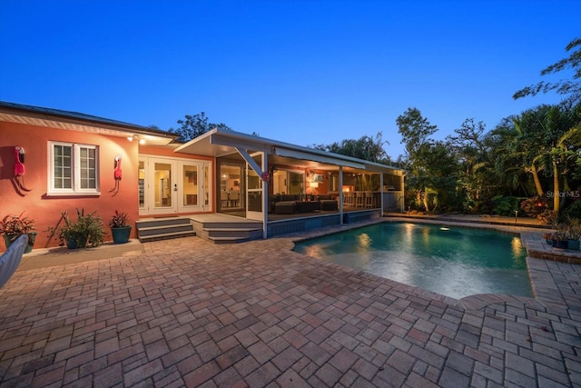 pool at dusk with french doors and a patio area