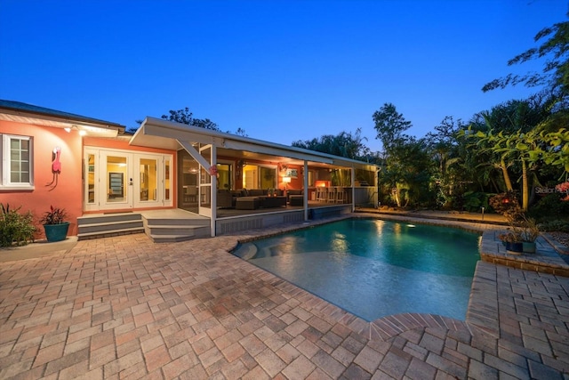 pool at dusk with outdoor lounge area, french doors, and a patio