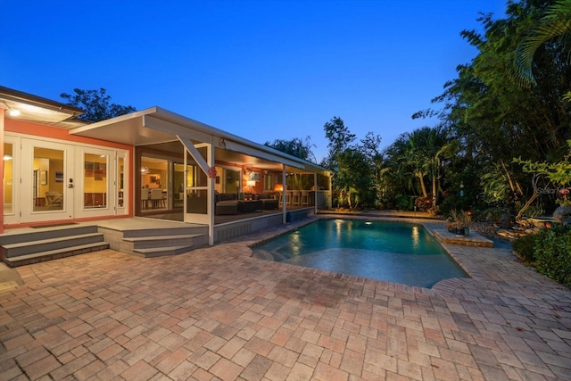 pool at dusk with french doors and a patio area