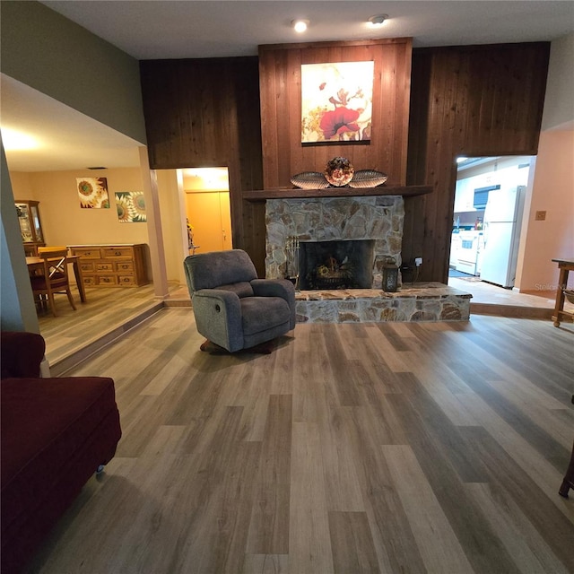 living room with wood-type flooring, wood walls, and a stone fireplace