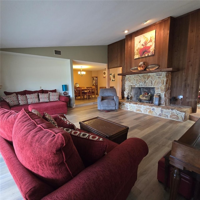 living room with an inviting chandelier, wood walls, light wood-type flooring, a fireplace, and vaulted ceiling