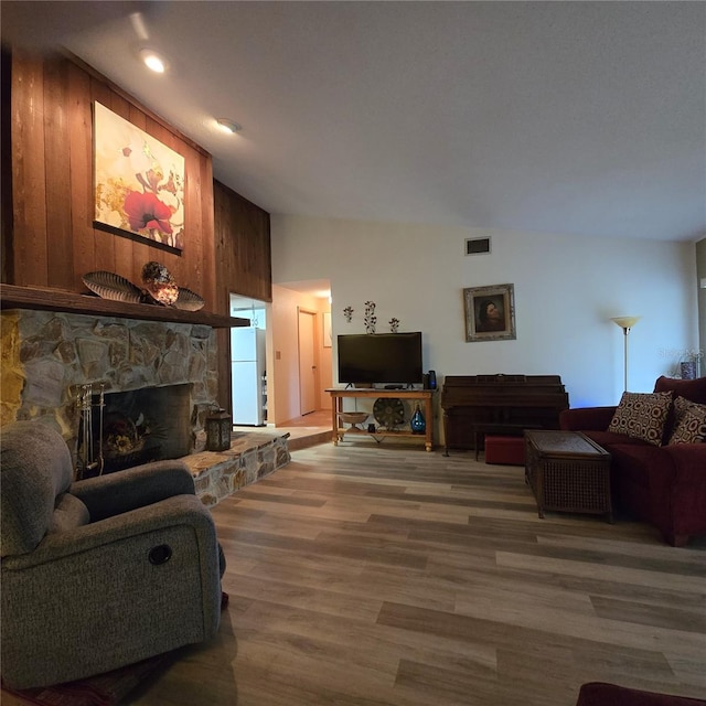 living room with hardwood / wood-style flooring, lofted ceiling, wood walls, and a stone fireplace