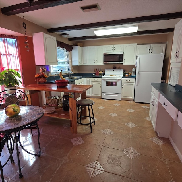 kitchen with light tile patterned floors, white cabinetry, white appliances, beam ceiling, and sink