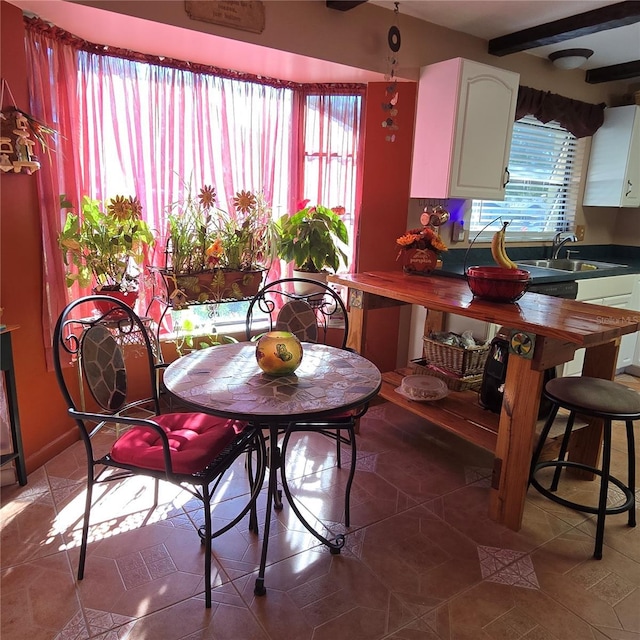 dining space with beamed ceiling, dark tile patterned flooring, and sink