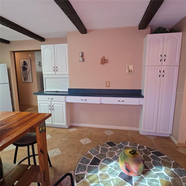 kitchen with white refrigerator, white cabinets, and beamed ceiling