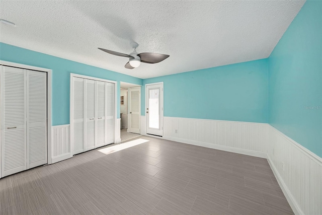 unfurnished bedroom with ceiling fan, a textured ceiling, and multiple closets