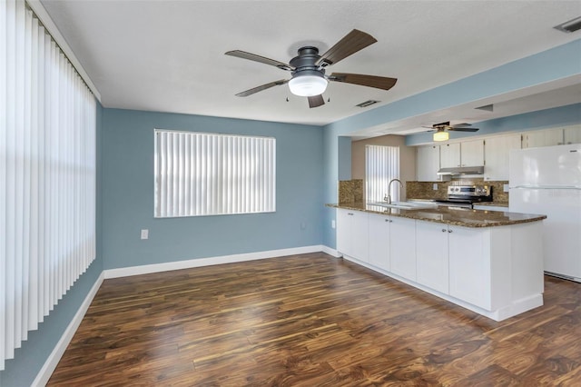 kitchen with dark hardwood / wood-style flooring, kitchen peninsula, dark stone countertops, white fridge, and stainless steel range with electric stovetop