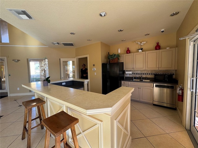 kitchen featuring dishwasher, black fridge, a kitchen island, a breakfast bar area, and light tile patterned flooring