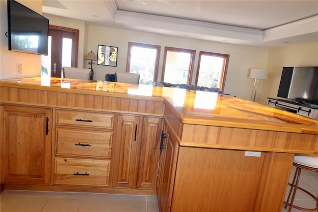 kitchen with wooden counters, ornamental molding, a breakfast bar, a raised ceiling, and light tile patterned floors