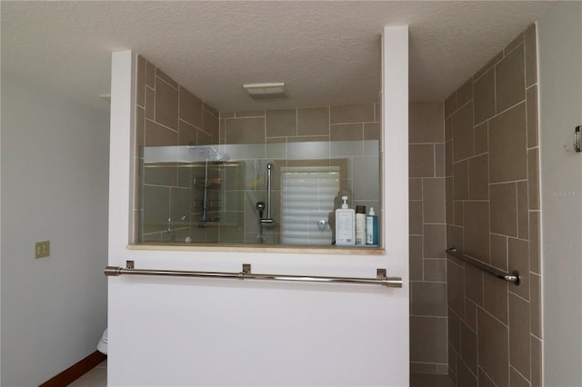 bathroom with tiled shower, a textured ceiling, and toilet