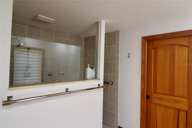 bathroom with a tile shower and a textured ceiling