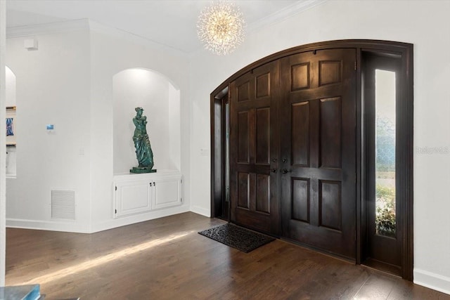 foyer with crown molding, dark wood-type flooring, and an inviting chandelier