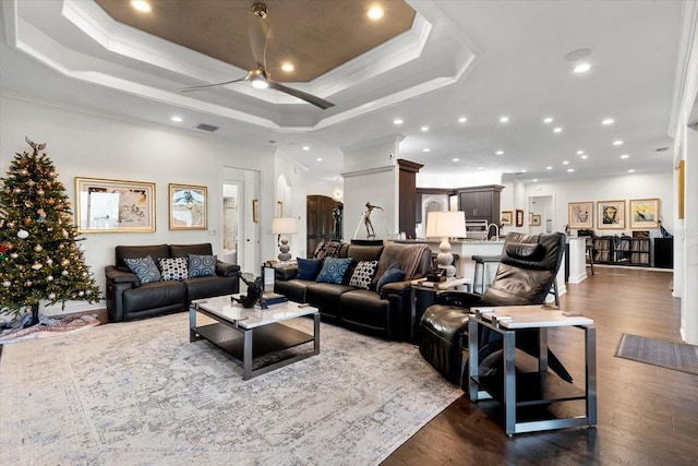 living room featuring a tray ceiling, ceiling fan, dark hardwood / wood-style floors, and ornamental molding