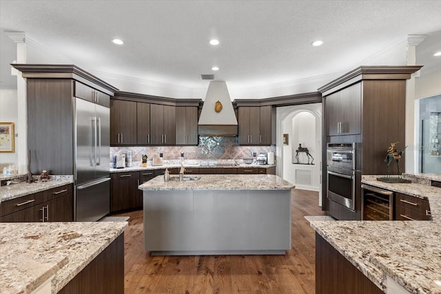 kitchen featuring dark brown cabinets, dark hardwood / wood-style floors, premium range hood, and stainless steel appliances