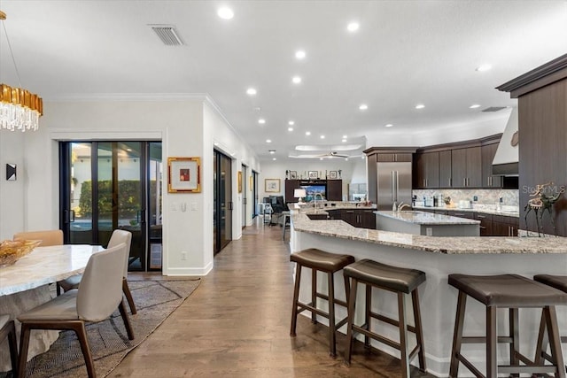 kitchen featuring dark brown cabinetry, light stone countertops, dark hardwood / wood-style flooring, decorative light fixtures, and stainless steel built in fridge