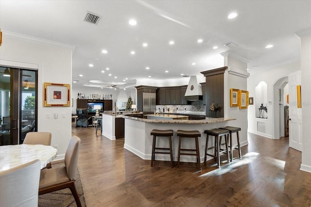 kitchen with ceiling fan, dark hardwood / wood-style floors, crown molding, a breakfast bar area, and dark brown cabinets