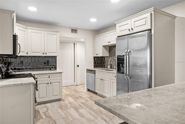 kitchen with decorative backsplash, white cabinetry, sink, and stainless steel appliances