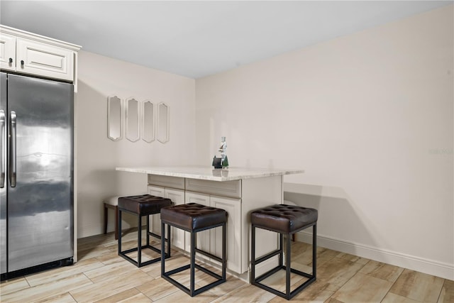 kitchen with light stone countertops, stainless steel fridge, light wood-type flooring, white cabinets, and a breakfast bar area