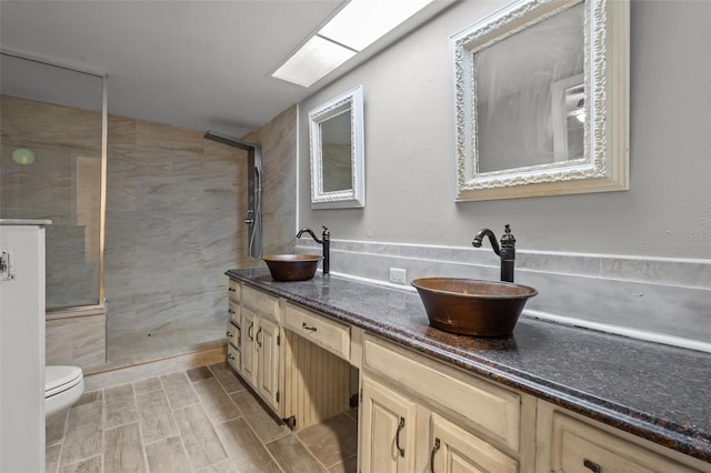 bathroom featuring a tile shower, a skylight, vanity, and toilet