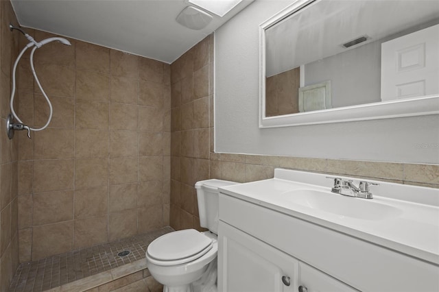 bathroom featuring a tile shower, vanity, tile walls, and toilet