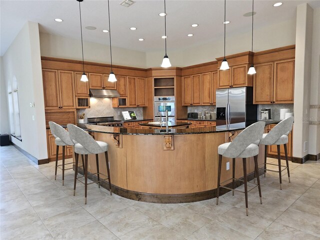 kitchen featuring appliances with stainless steel finishes, a kitchen breakfast bar, a large island with sink, dark stone countertops, and hanging light fixtures