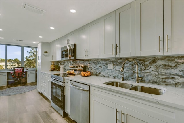 kitchen with appliances with stainless steel finishes, light stone counters, sink, light hardwood / wood-style flooring, and white cabinetry