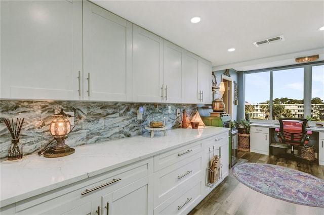 kitchen with white cabinets, backsplash, light stone counters, and dark wood-type flooring